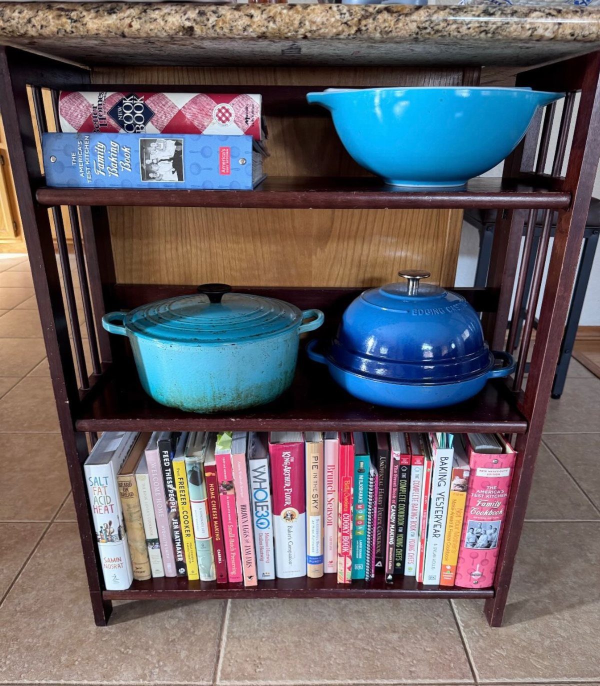 Dark wood shelves holding blue bowls, Dutch ovens, and many colorful cookbooks.
