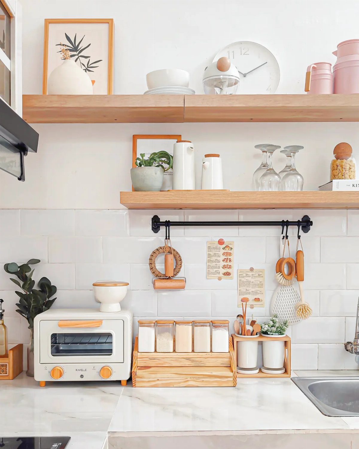 Wooden open shelves displaying coordinated white ceramics, pink mugs, and natural textures against white tiles.