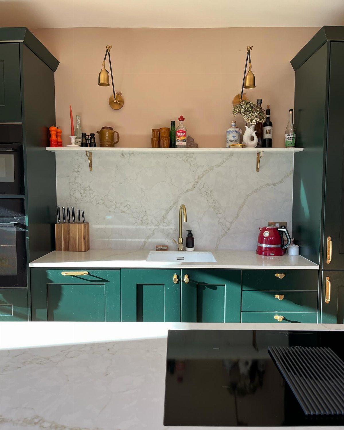 A white marble shelf holding kitchen items sits above a sink and marble backsplash.