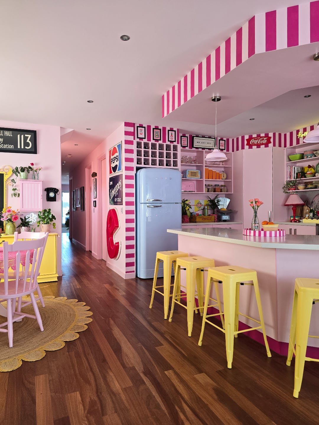 Pink kitchen with striped walls, light blue refrigerator, and yellow stools around a counter.