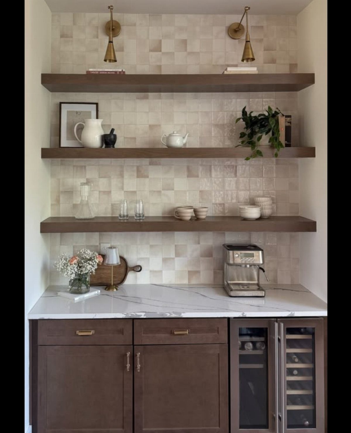 Dark wood floating shelves with brass wall sconces and white ceramic decor on a tiled backsplash.