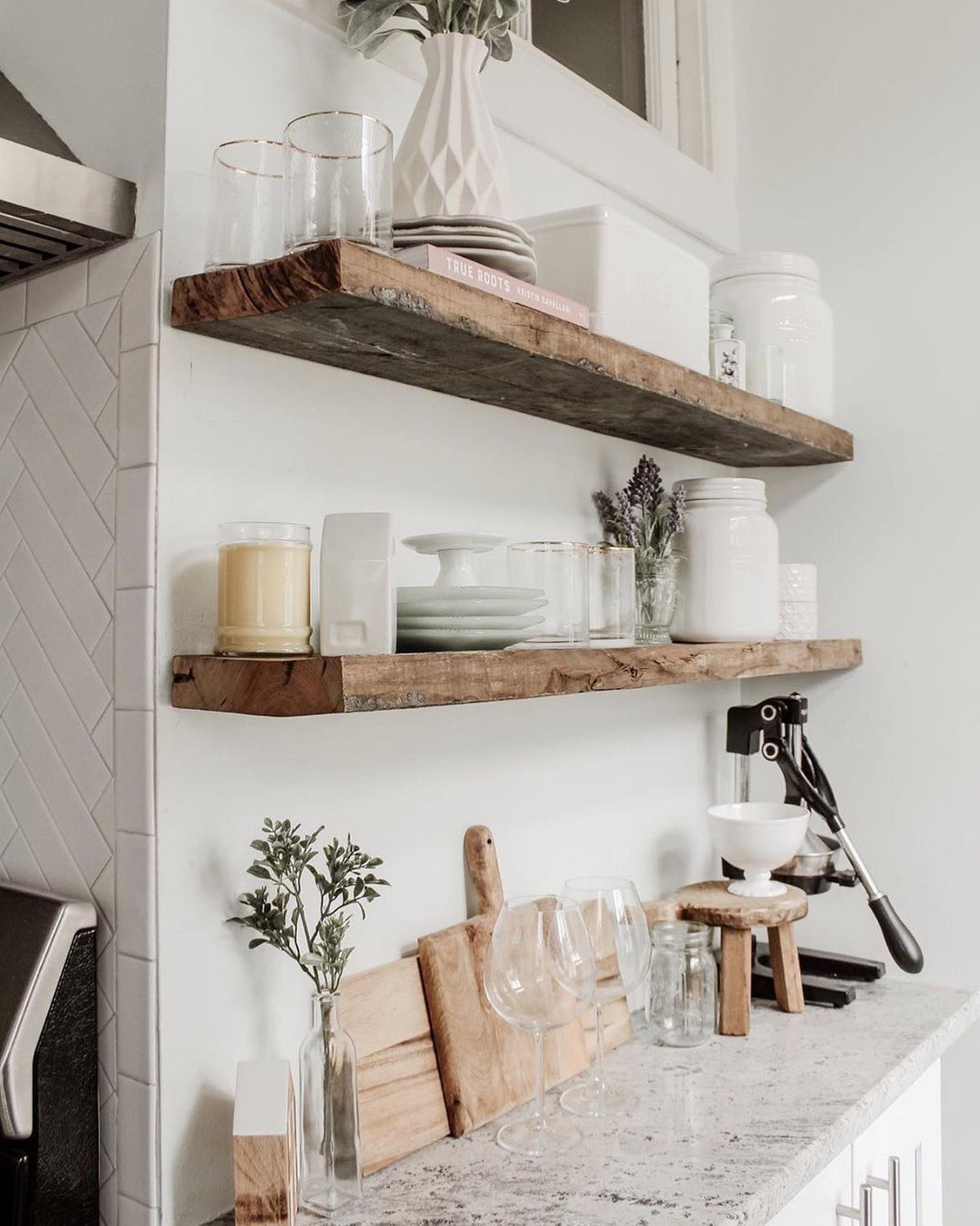 Rustic wooden floating shelves holding white ceramics and glassware against a white kitchen wall.