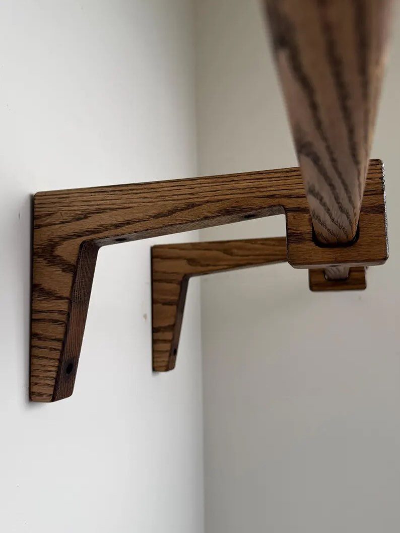 A dark wood geometric bracket supporting a wooden shelf against a white wall.