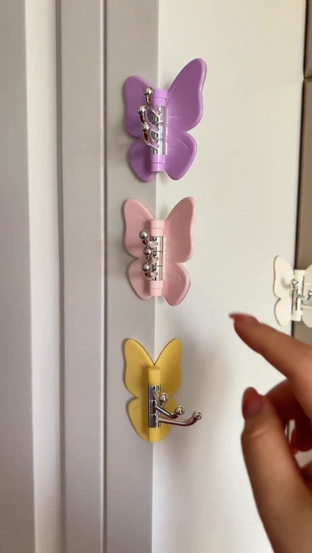 Butterfly-shaped wall hooks in purple, pink, and yellow mounted on a white door.