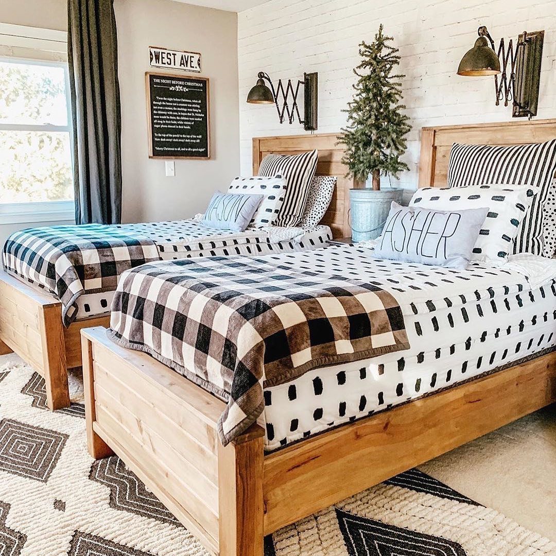 Two wooden twin beds with patterned bedding and black articulated arm sconces on a white brick wall.