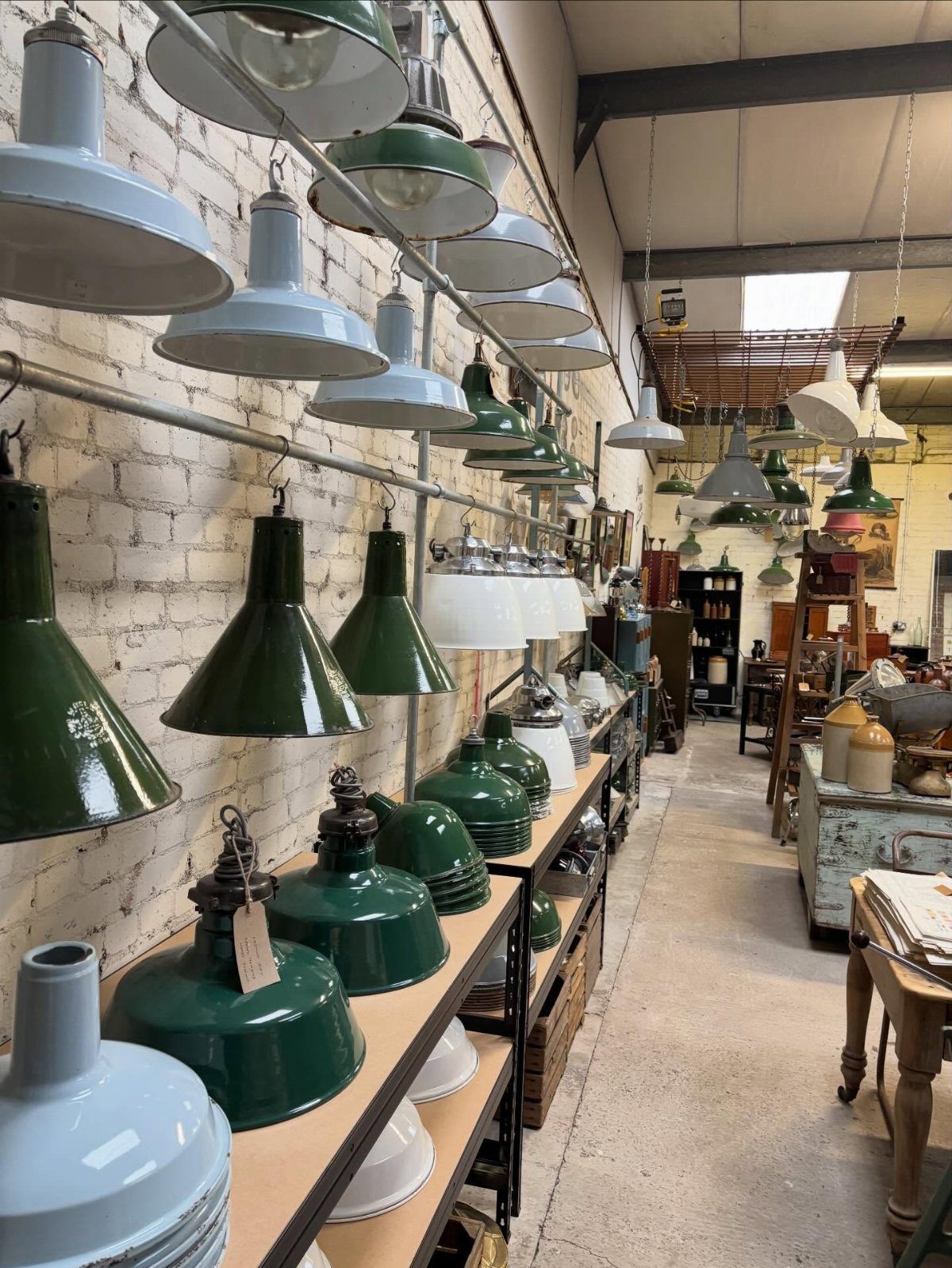 Rows of green and white industrial pendant lamps displayed on shelves against a brick wall.