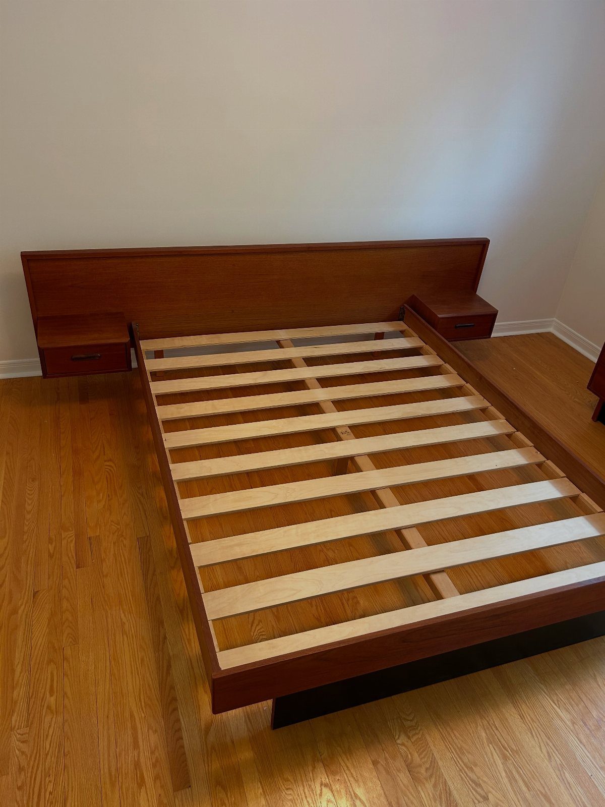 A wooden bed frame with integrated nightstands on a light wood floor.