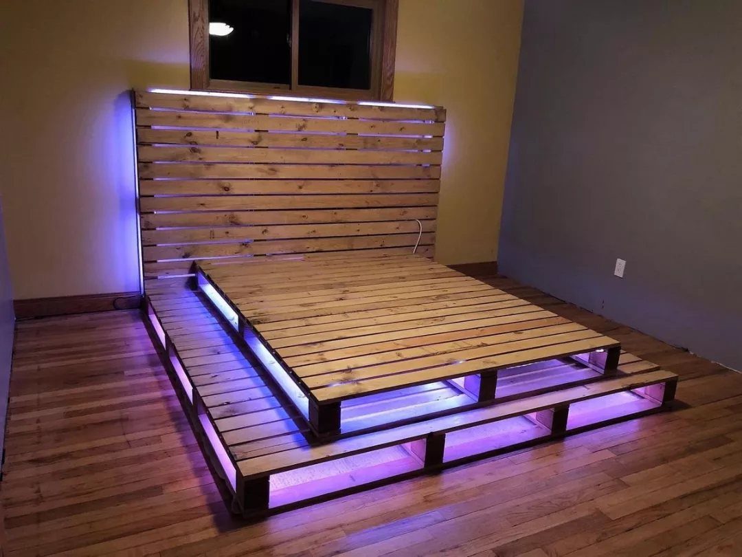 Wooden pallet bed frame with glowing purple LED lights underneath the platform and headboard.