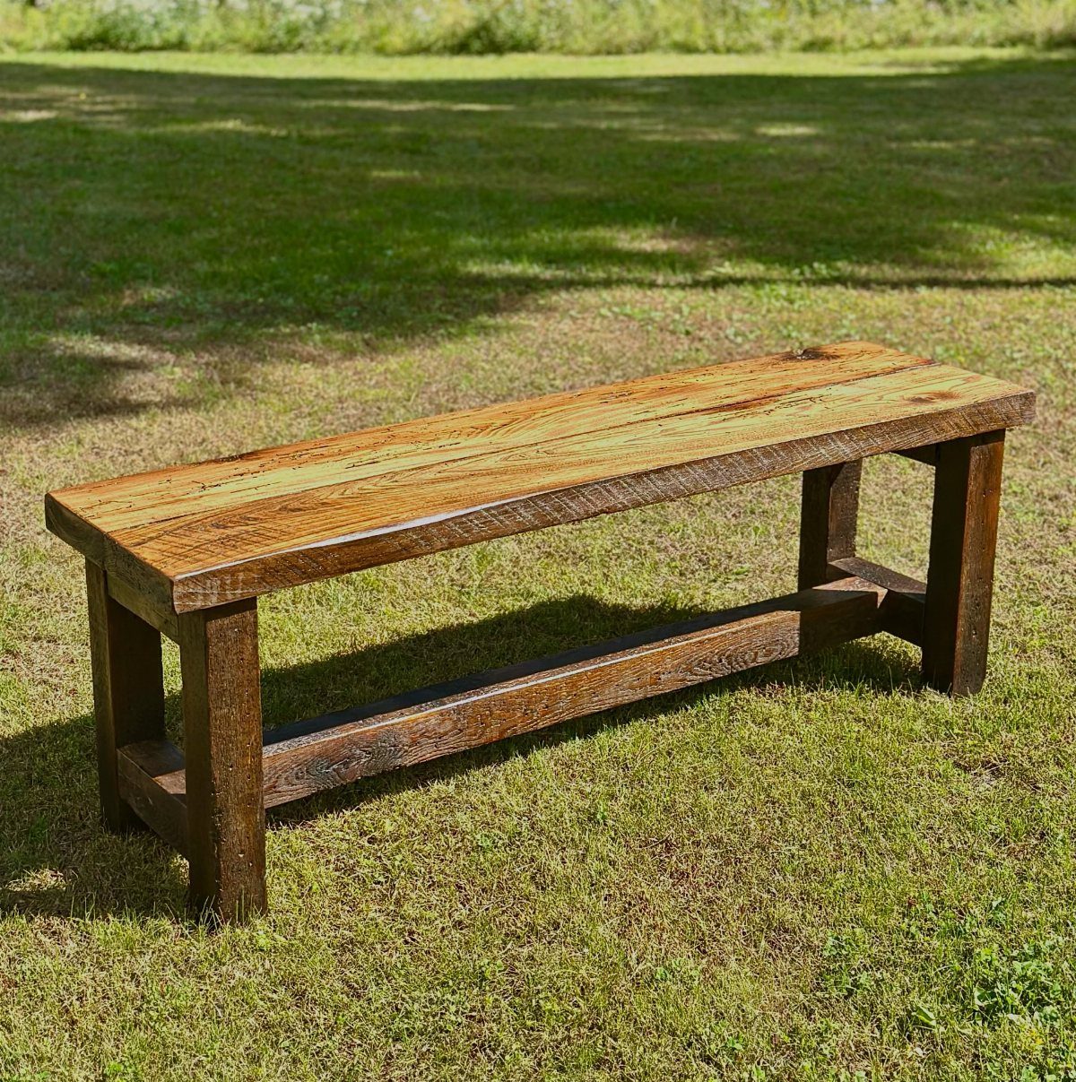 A long rustic bench made of reclaimed wood sitting on a green grass lawn.