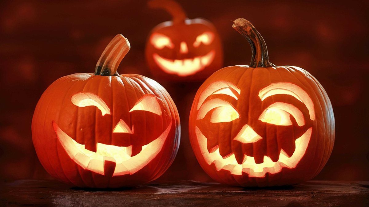 Three glowing carved jack-o'-lanterns with various facial expressions sitting on a dark wooden surface.