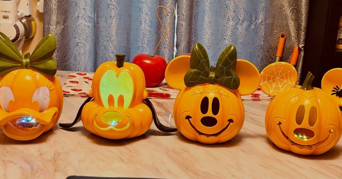 Four orange Mickey Mouse themed plastic pumpkins lined up on a kitchen counter.