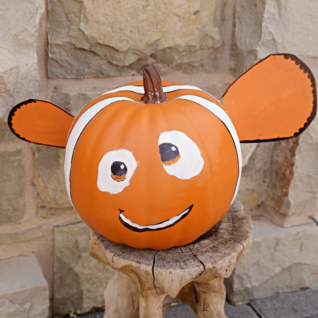 Painted Nemo pumpkin with white stripes and fins sitting on a wooden stump.