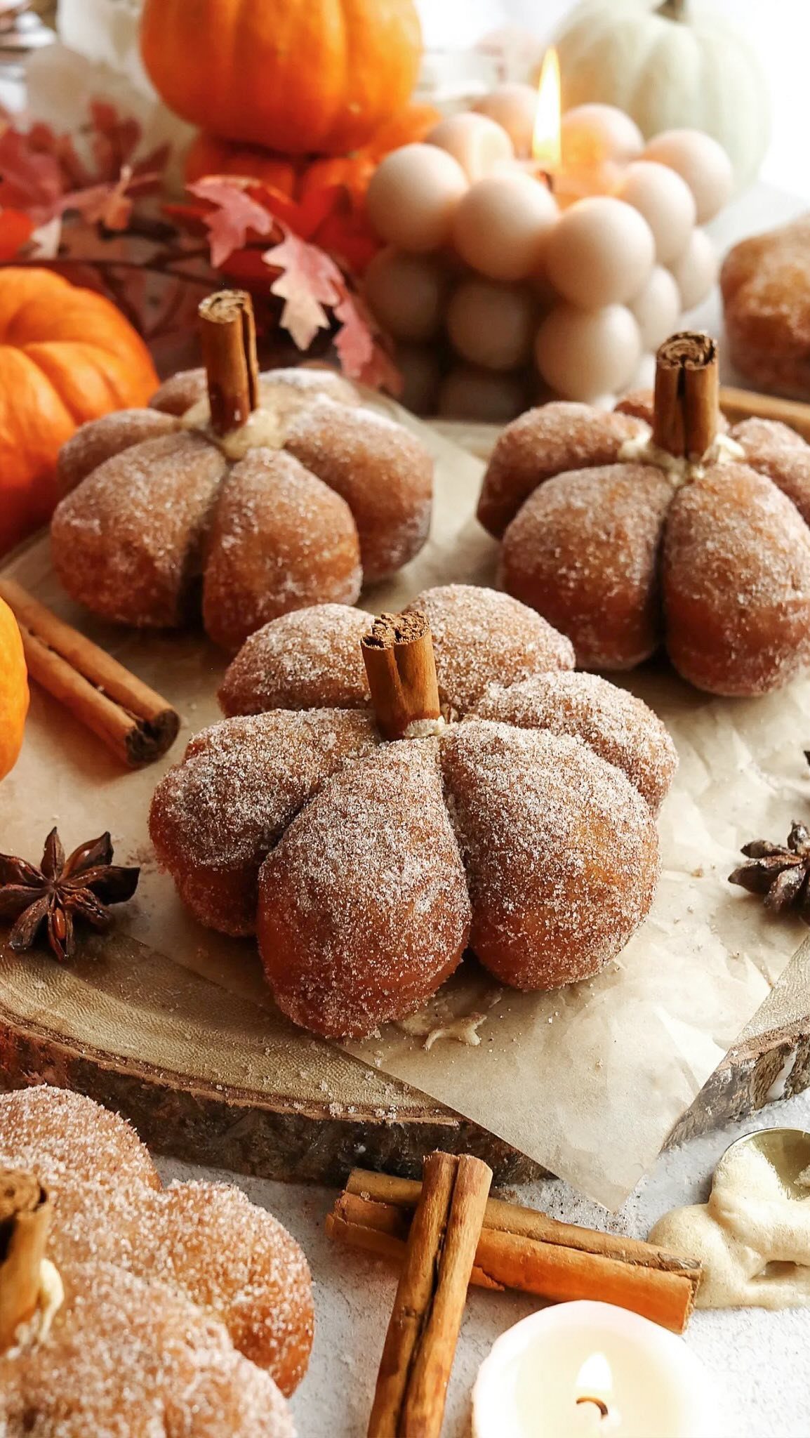 Sugar-coated pumpkin-shaped pastries arranged with cinnamon sticks and star anise on parchment paper.