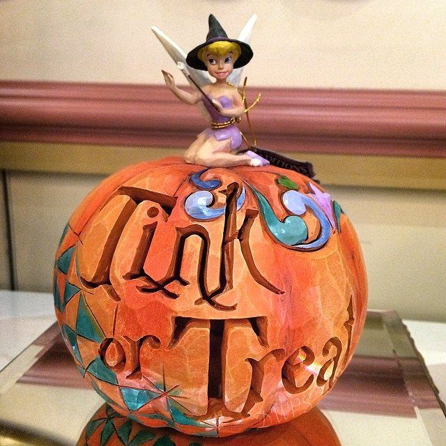 Carved orange pumpkin with Tink or Treat text and a Tinker Bell figurine on top.