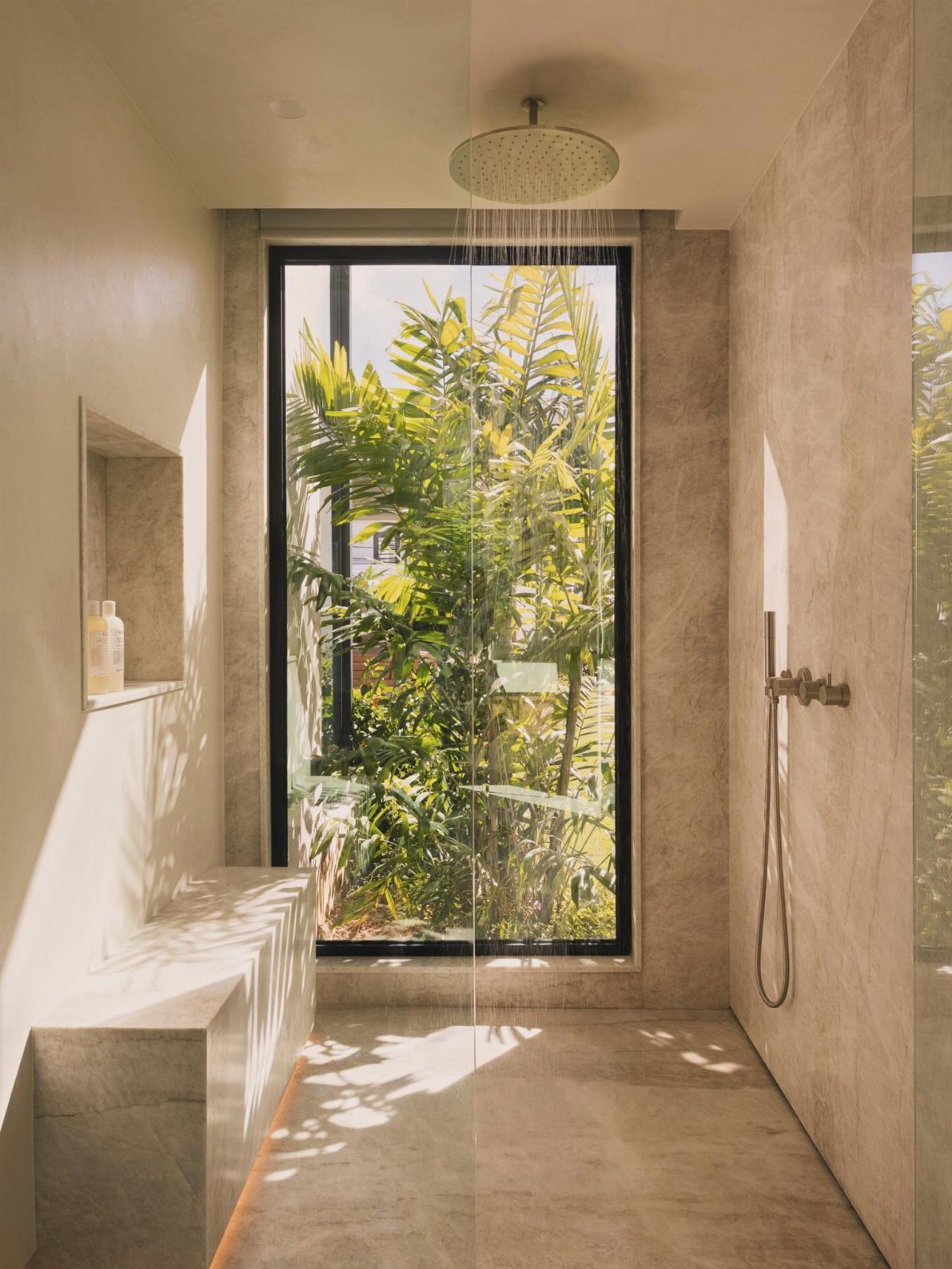 Sunlit modern bathroom with a large window overlooking tropical green foliage and stone textures.
