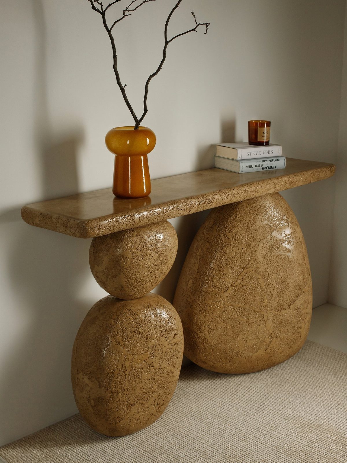A textured beige stone console table with large boulder-shaped legs holding a vase and books.
