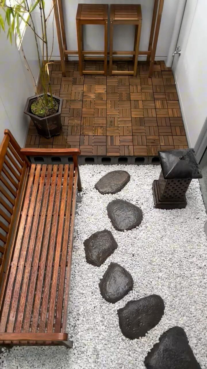 Zen garden with white gravel, dark stepping stones, wooden bench, and bamboo plant.