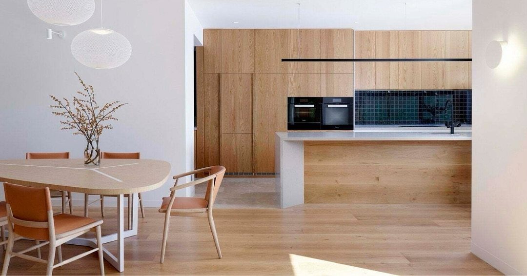 Light wood dining table and chairs set against a modern kitchen with wooden cabinetry.