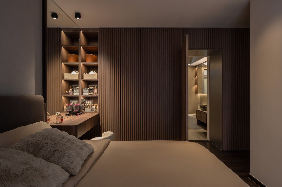 Modern bedroom with dark wood slatted walls, lit shelving, and neutral bedding.