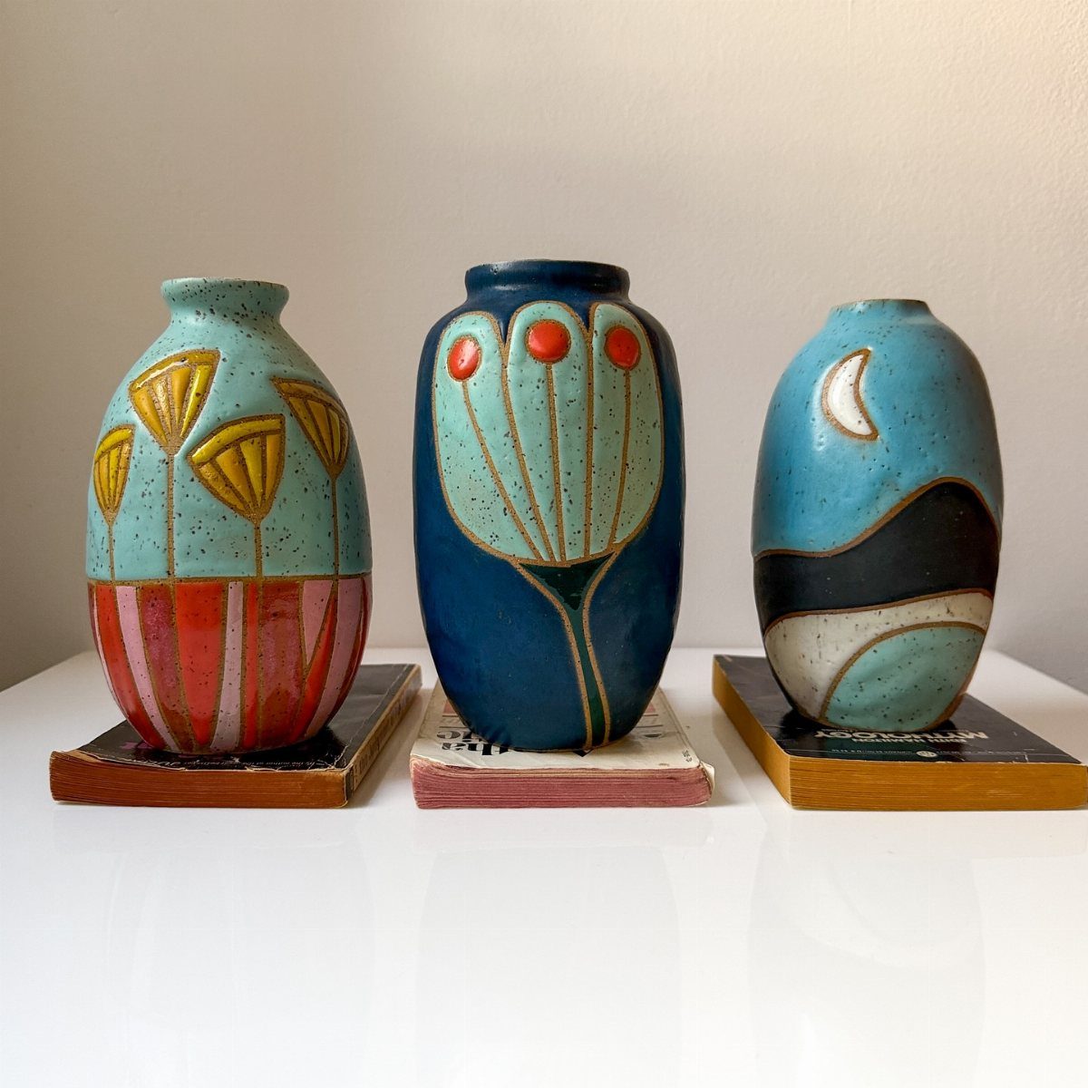 Three decorative ceramic vases with colorful patterns resting on small wooden bases.