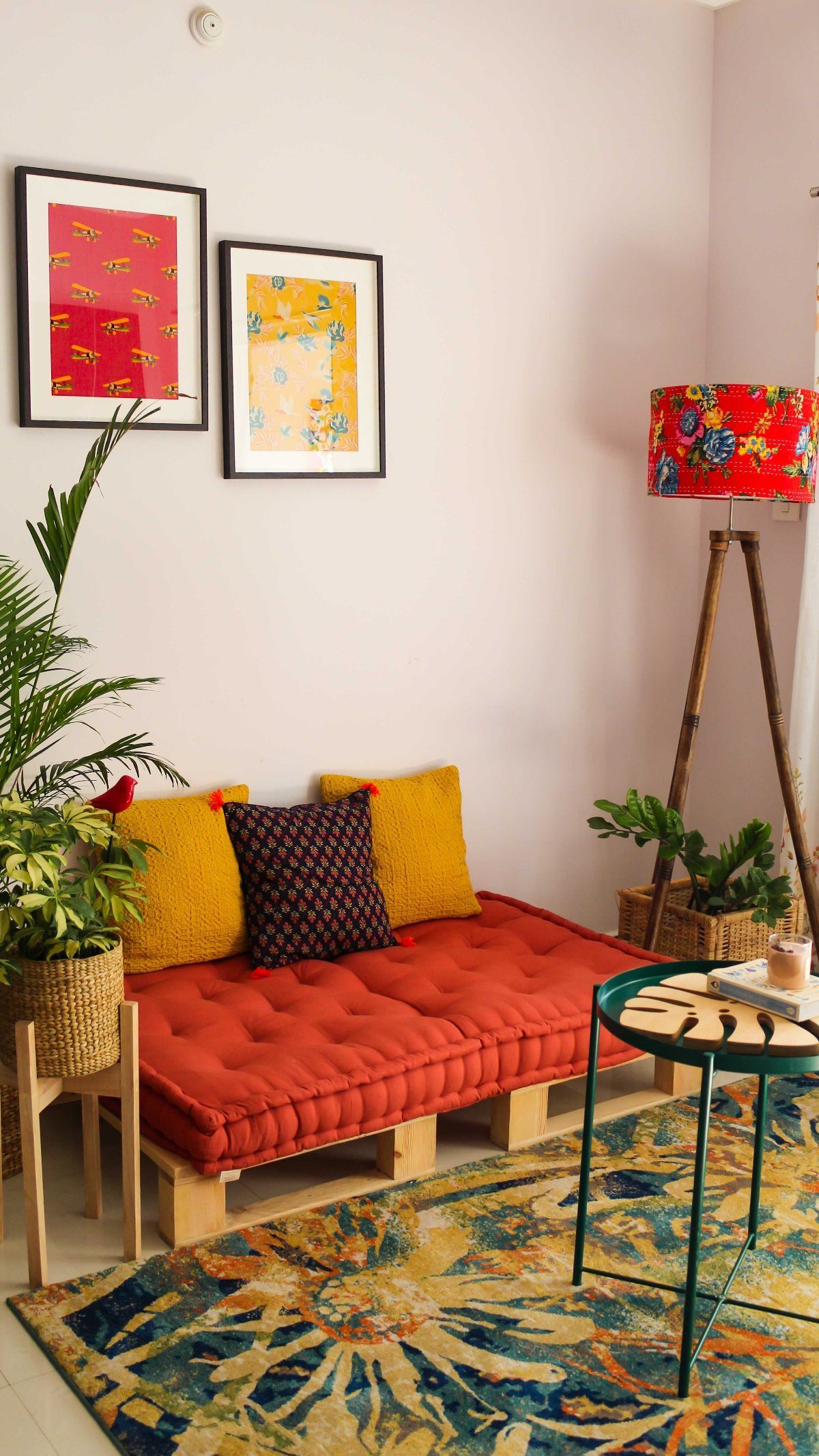 Low wooden platform daybed with red cushions and yellow pillows in a colorful living room.