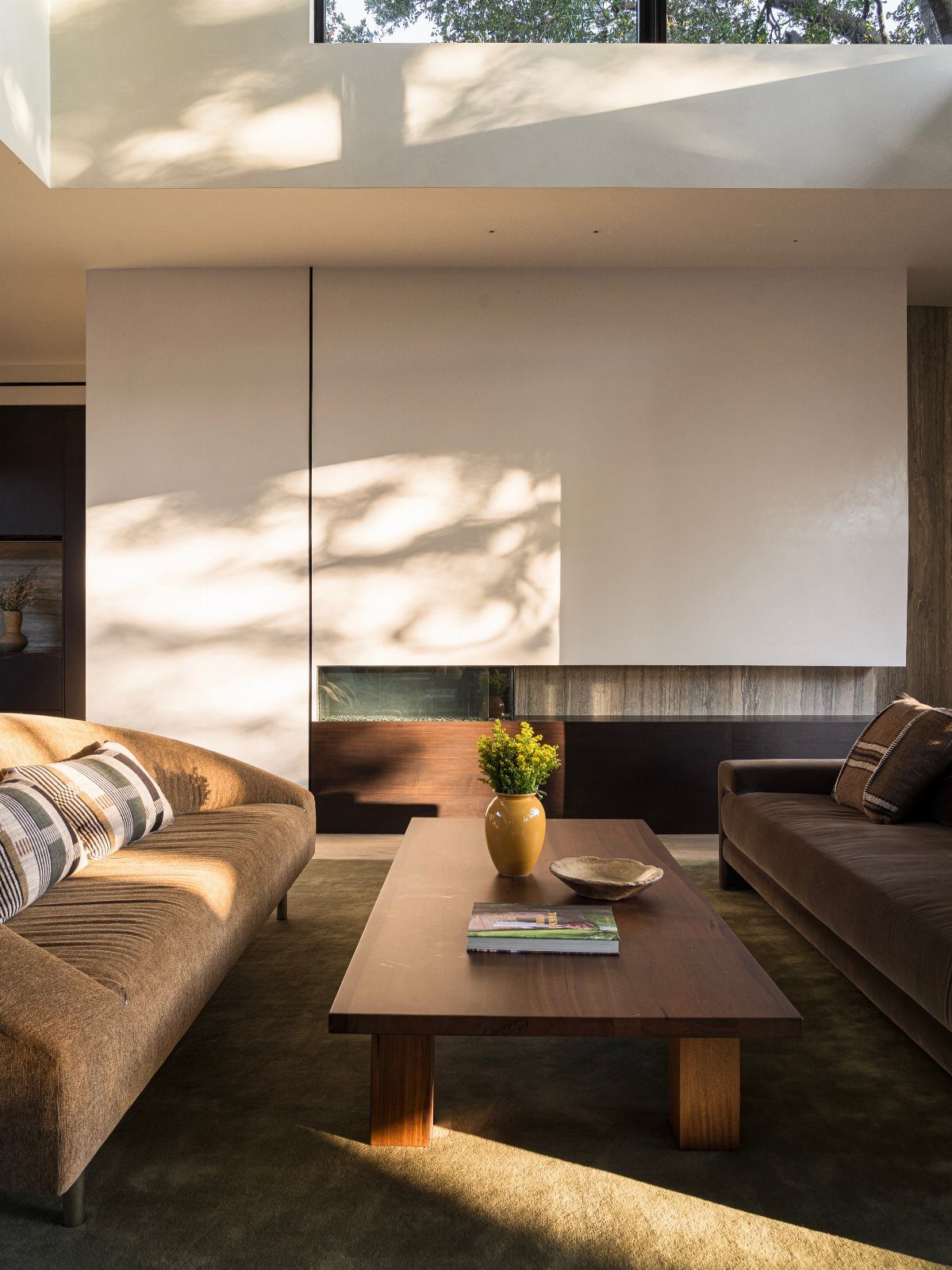 Sunlight streaming through a high window onto brown sofas and a wooden coffee table.