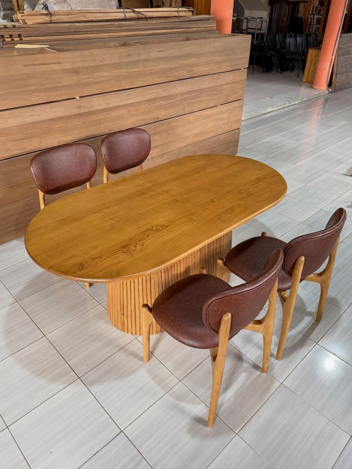 Oval wooden dining table with fluted base and four brown leather chairs on tile.