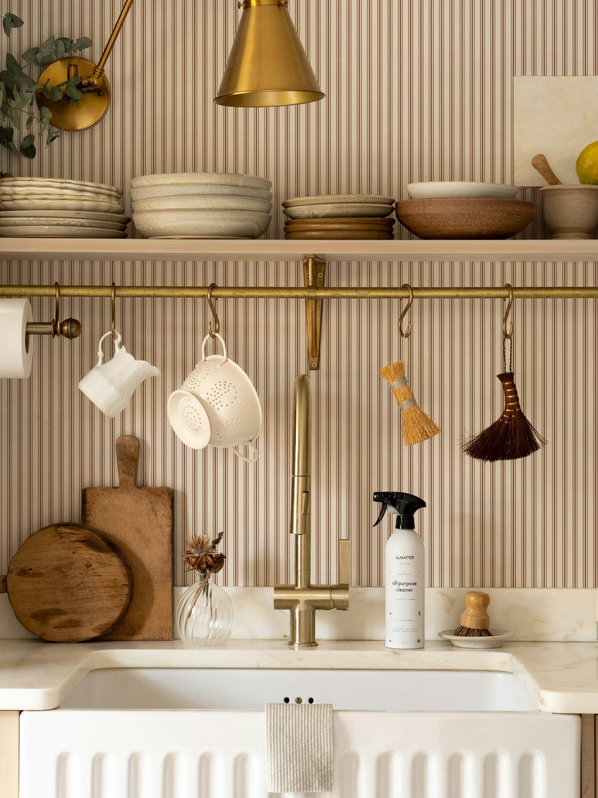Vertical beige striped wallpaper behind a brass kitchen faucet and open wooden shelving.