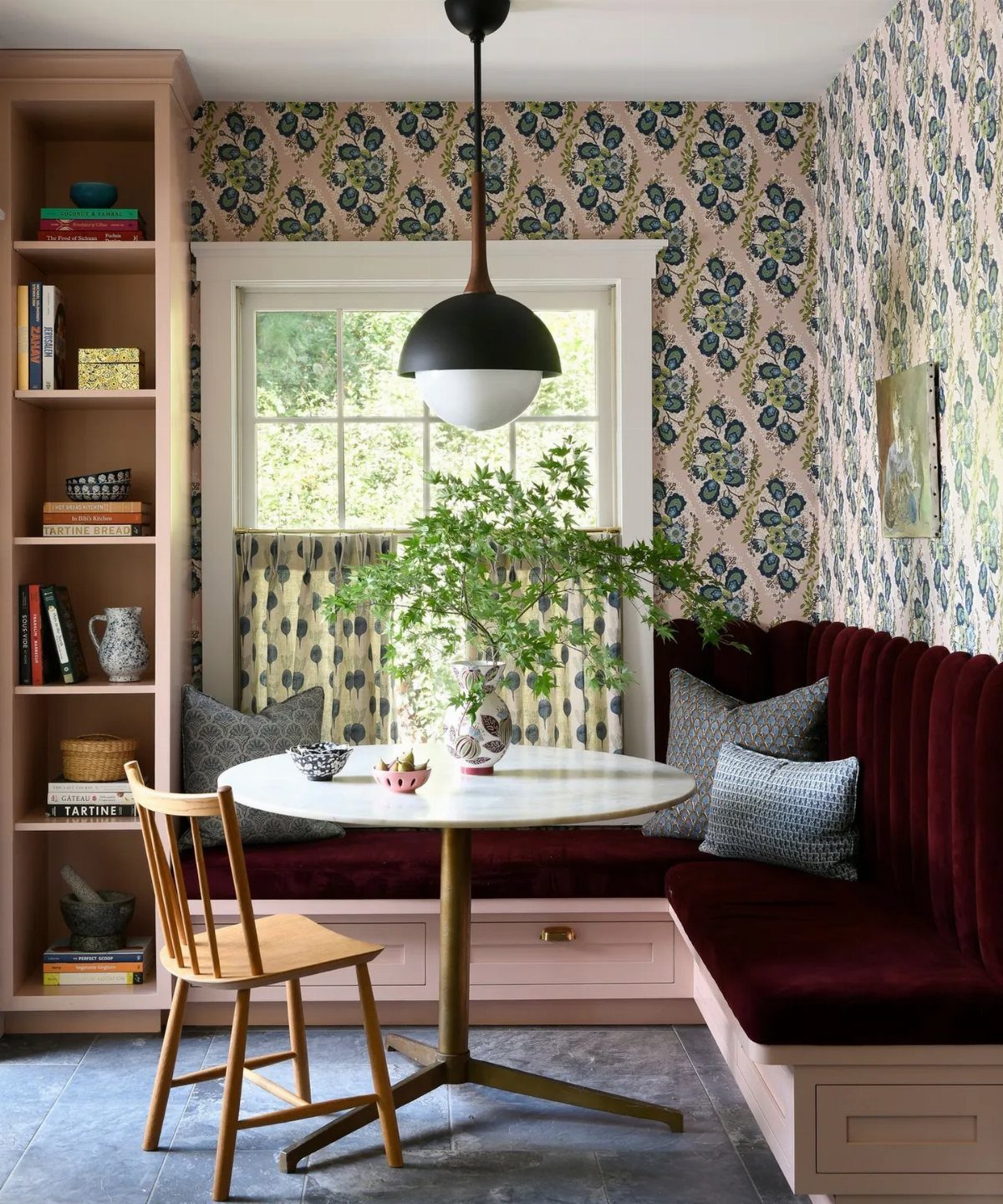 A breakfast nook with burgundy velvet seating, a marble table, and floral botanical wallpaper.