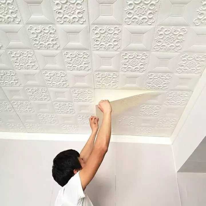A man installing white textured 3D patterned tiles onto a ceiling.