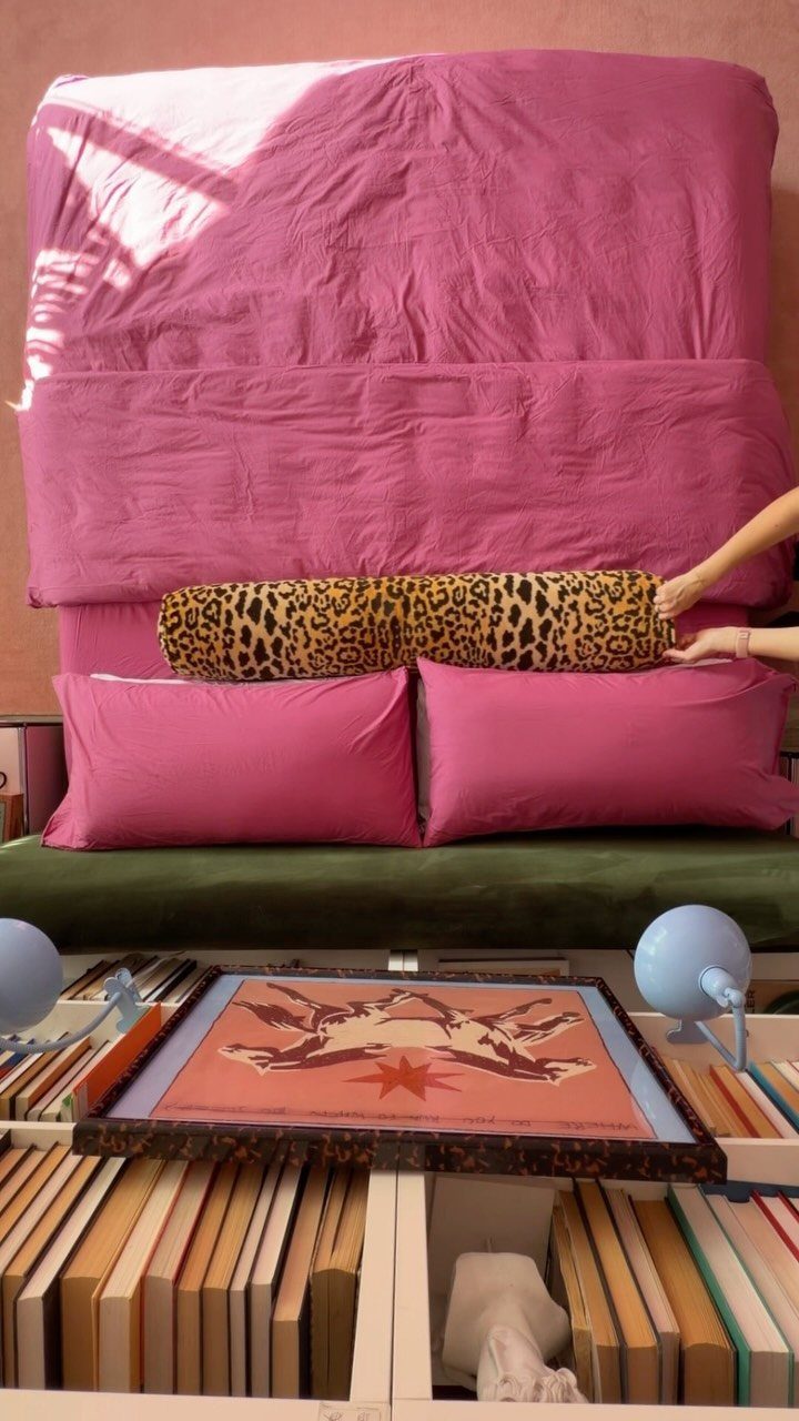Hands placing a leopard print bolster pillow onto a bed with pink pillows.