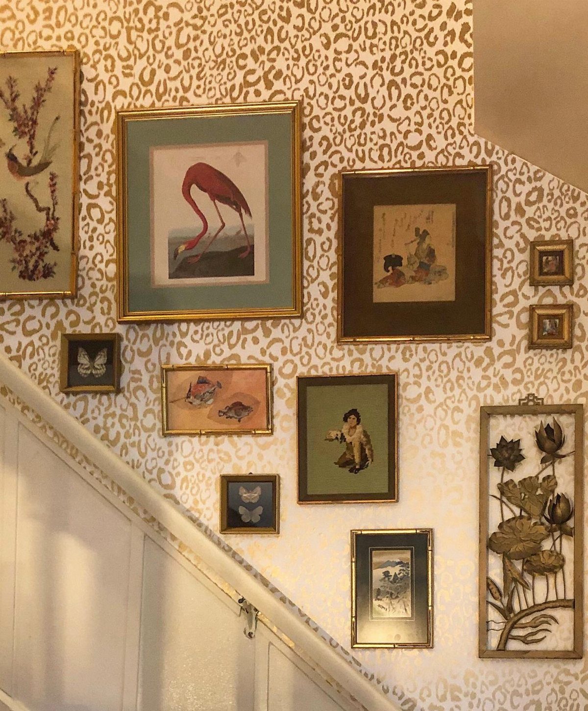 Framed artworks of animals and plants hanging on a gold leopard print wallpapered wall.