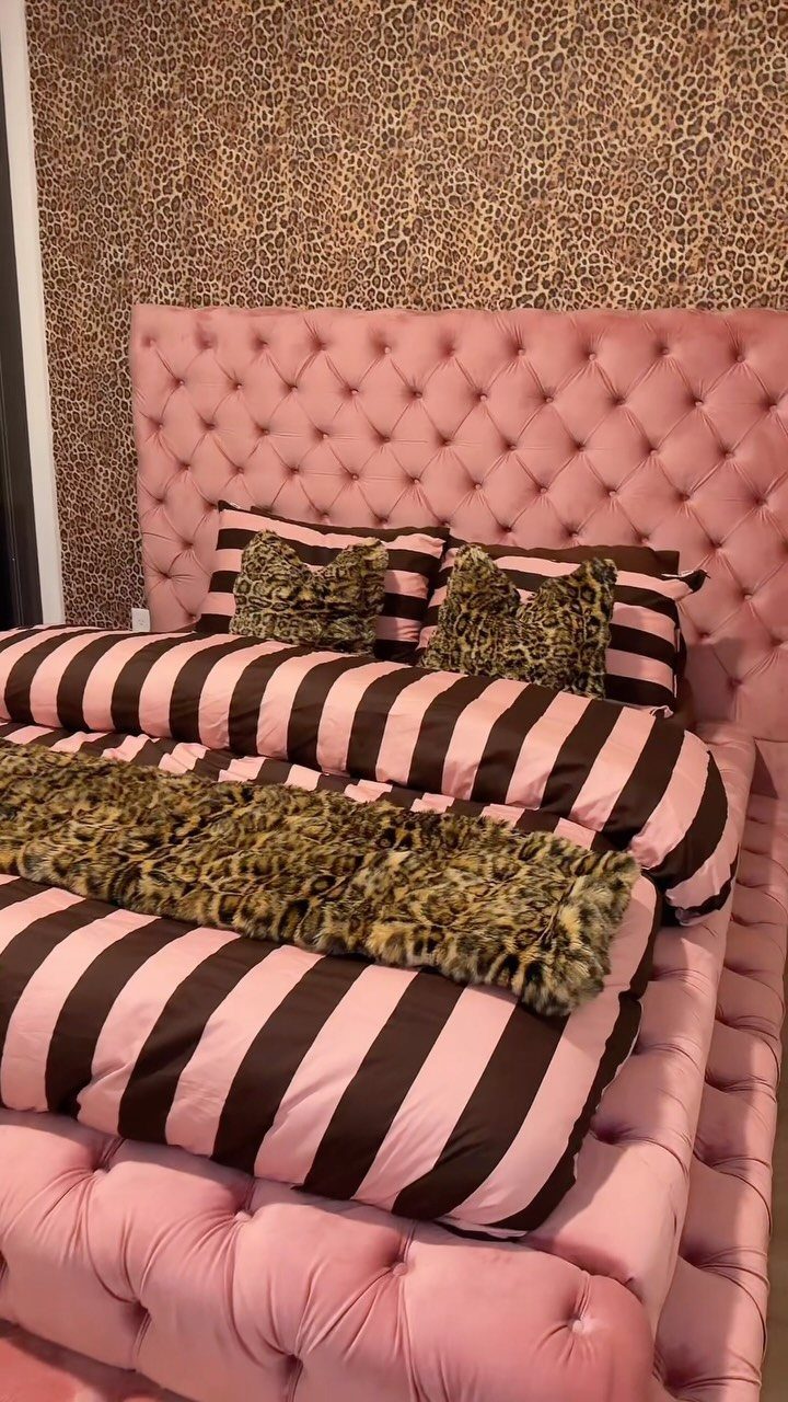A bed with pink tufted furniture, striped bedding, and leopard print pillows and throw.