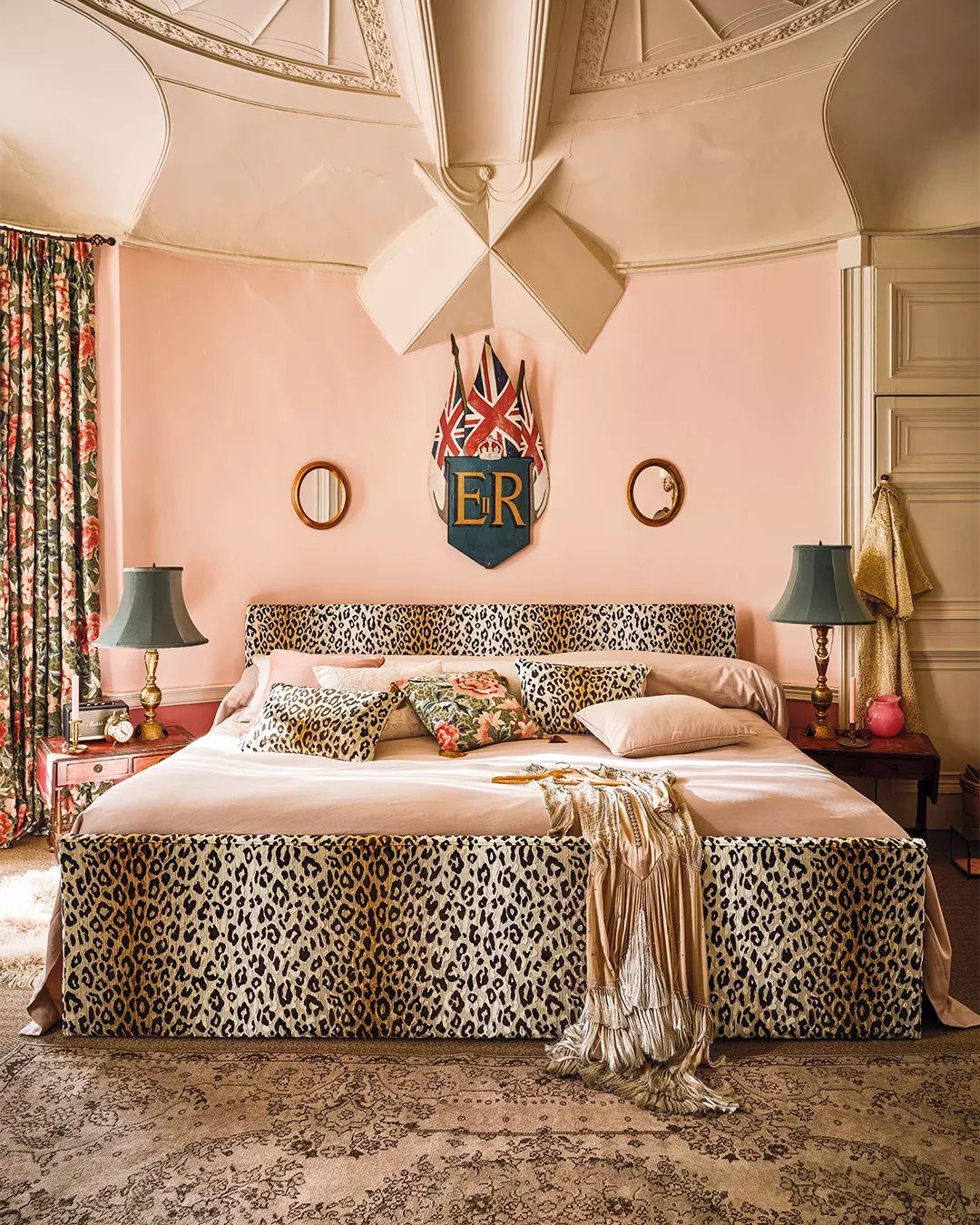 Leopard print upholstered headboard and matching bed skirt on a bed in a pink bedroom.
