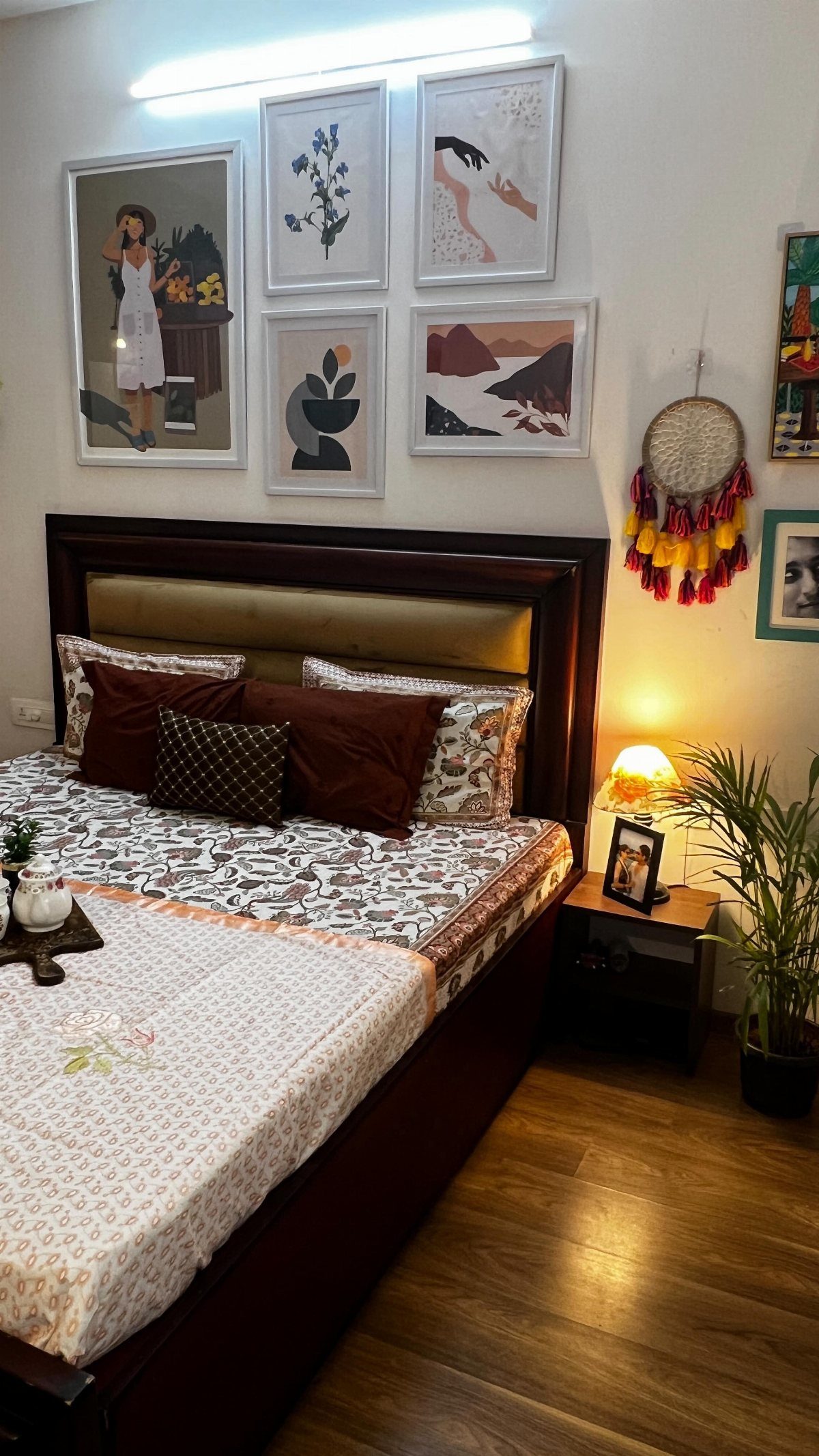 Framed art prints arranged on a white wall above a dark wood bed headboard.