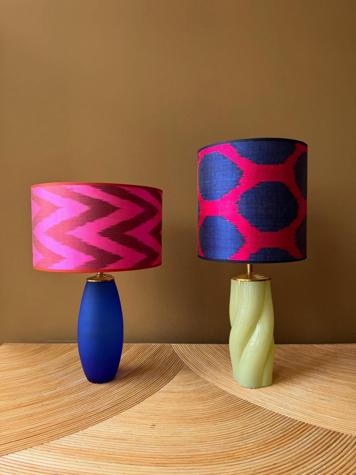 Two colorful patterned table lamps with unique blue and green bases on a wooden surface.
