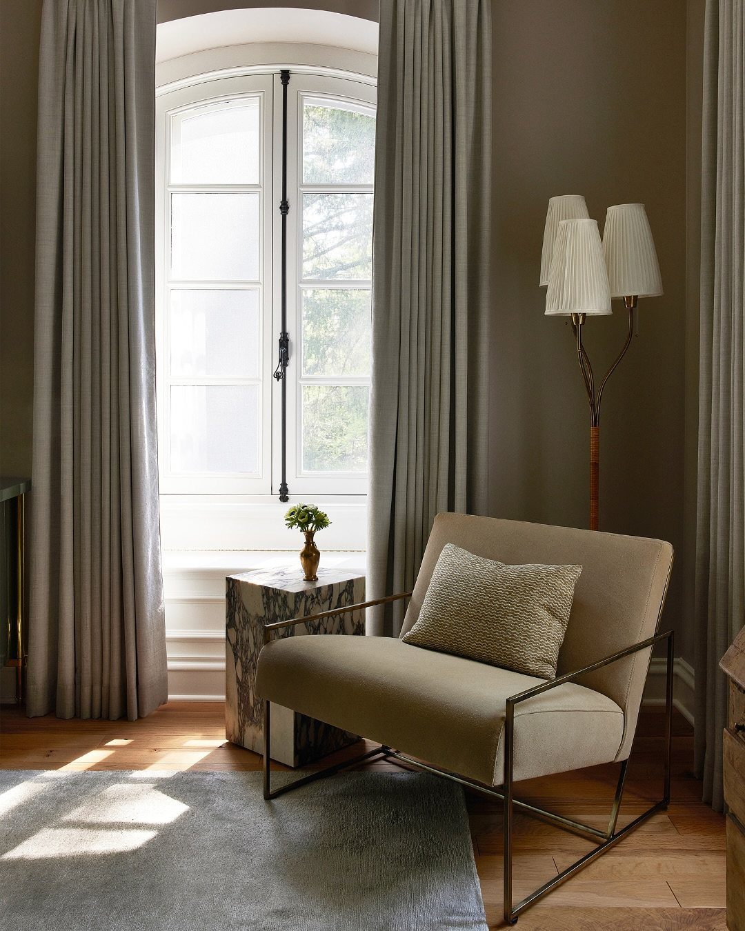Beige armchair and marble table positioned near a window and a pleated fabric floor lamp.