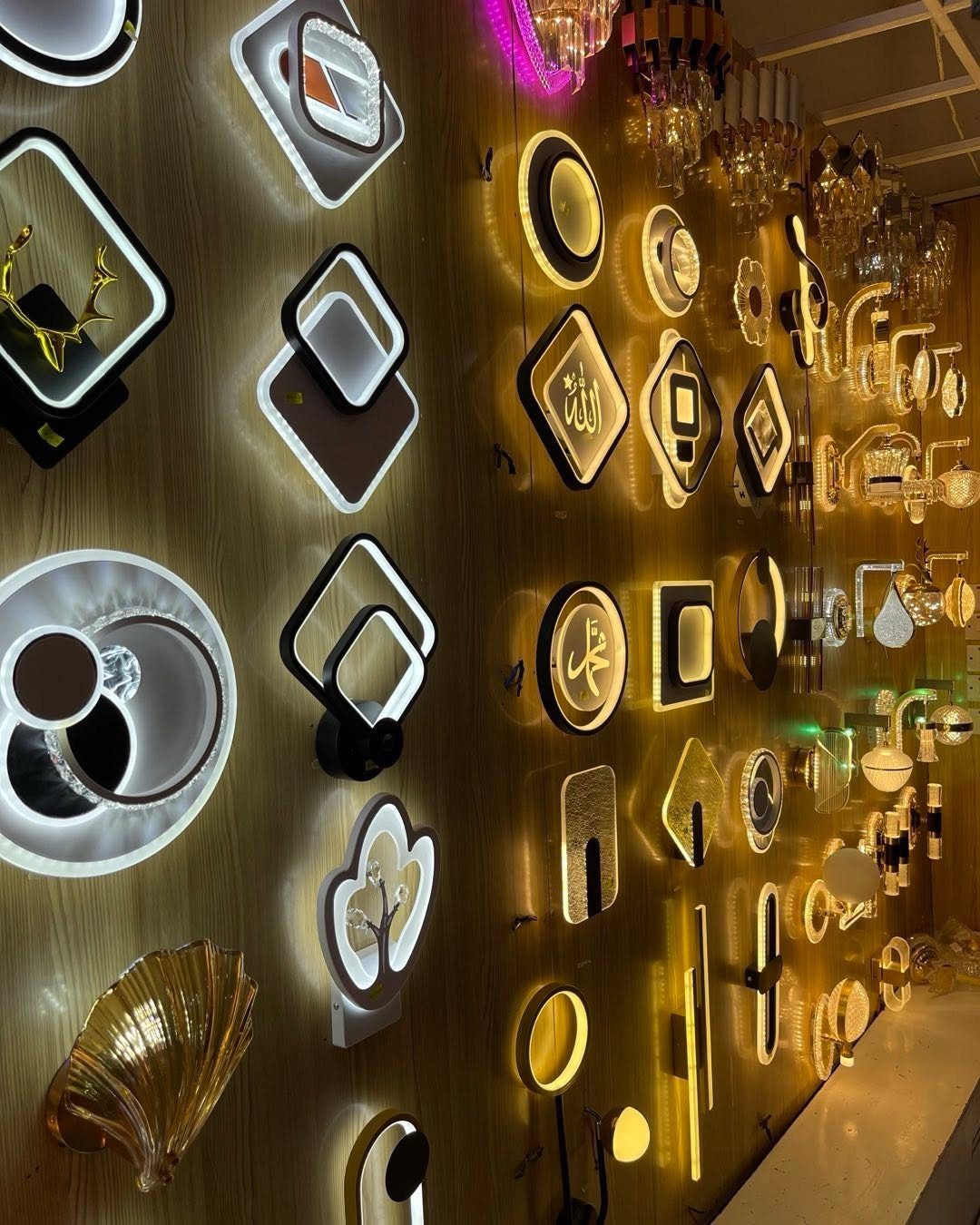 Various illuminated geometric wall sconces displayed on a wooden showroom wall.