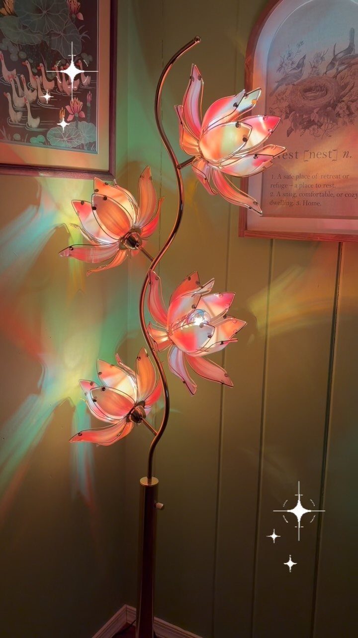 A curved floor lamp with glowing lotus flower shades casting colorful light on a green wall.