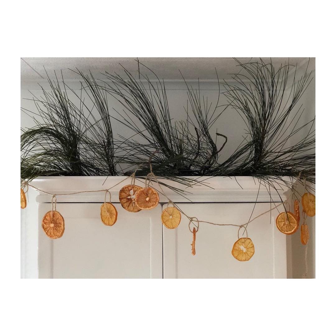 Dried orange slices on a twine garland hanging across a white mantel with pine needles.