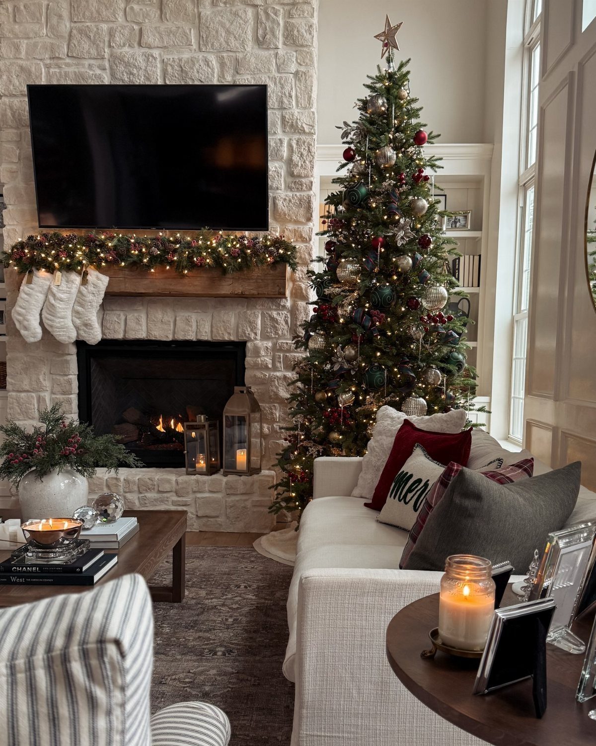 A decorated living room with a lit fireplace, Christmas tree, and textured pillows on a white sofa.