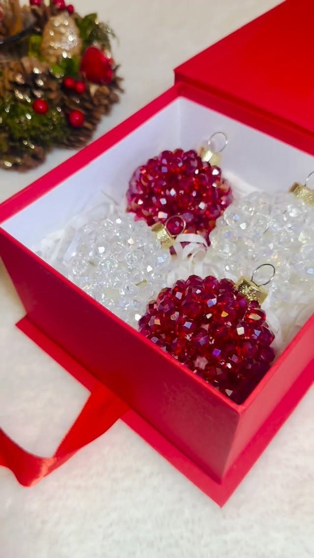 Red and white beaded Christmas ornaments nestled inside a bright red gift box.