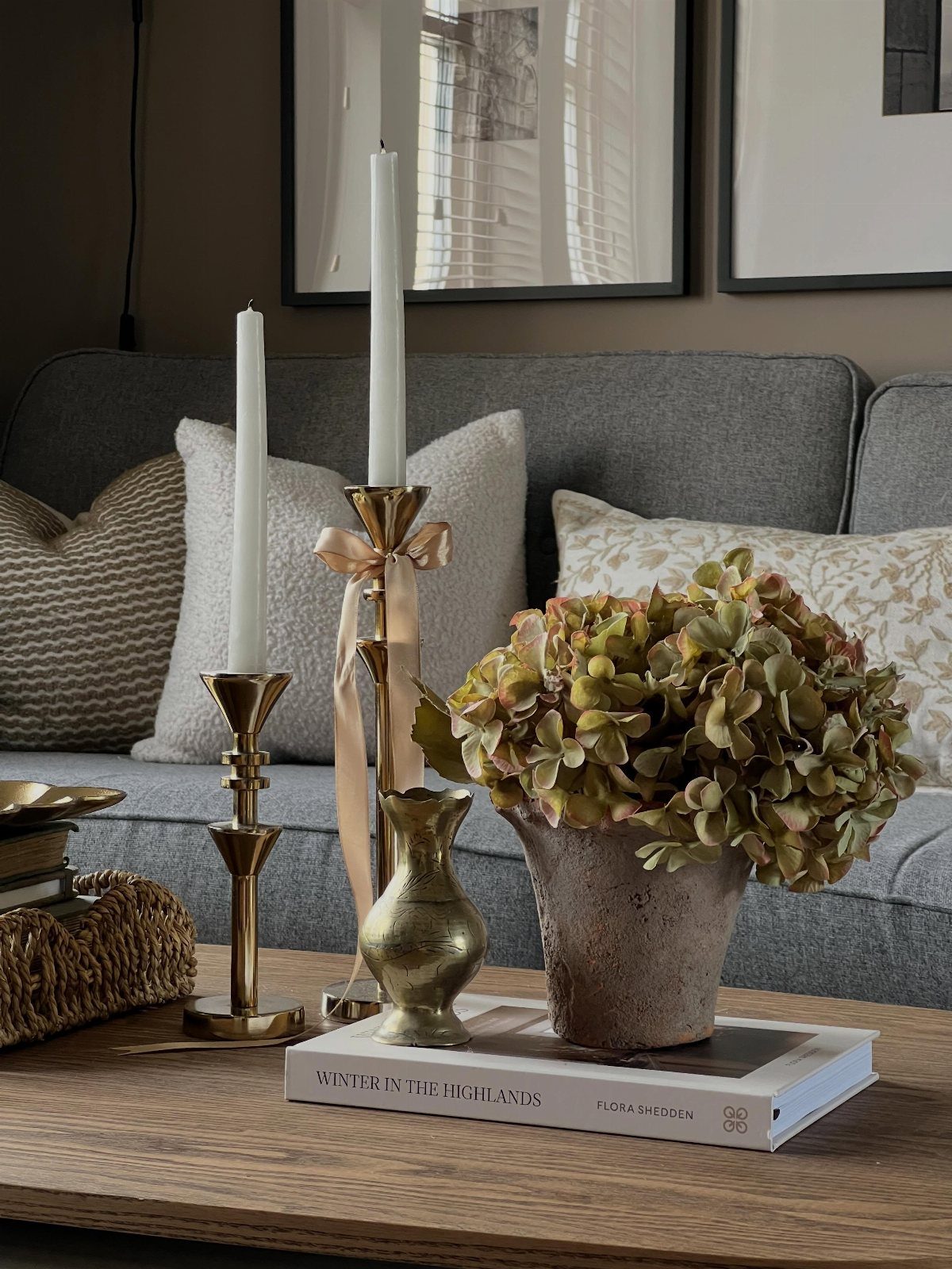 Gold candlesticks, a small vase, and hydrangeas arranged on a wooden coffee table.