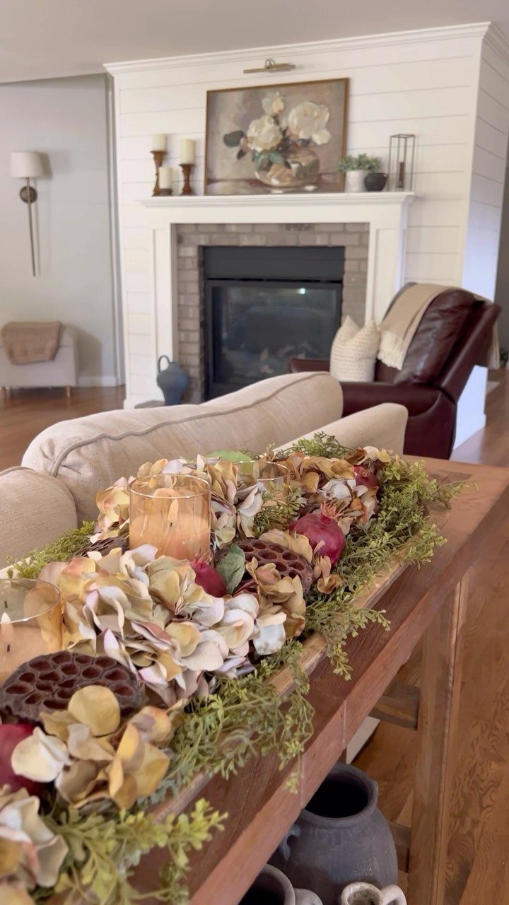 A wooden dough bowl centerpiece filled with dried florals and greenery on a coffee table.
