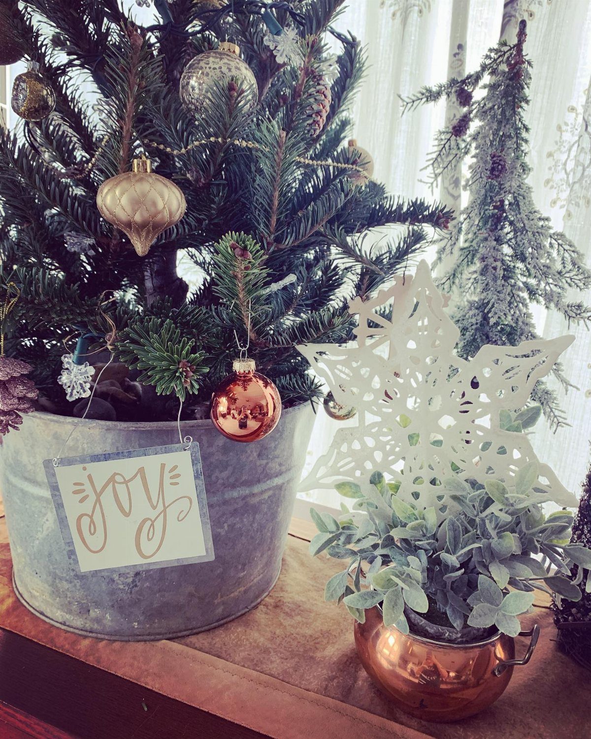 A decorated Christmas tree inside a large galvanized metal bucket with a JOY sign.