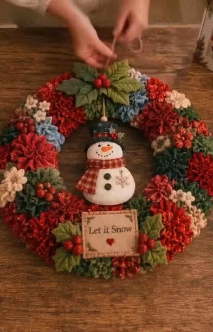 Hands holding a colorful fabric wreath decorated with a snowman and holly leaves.