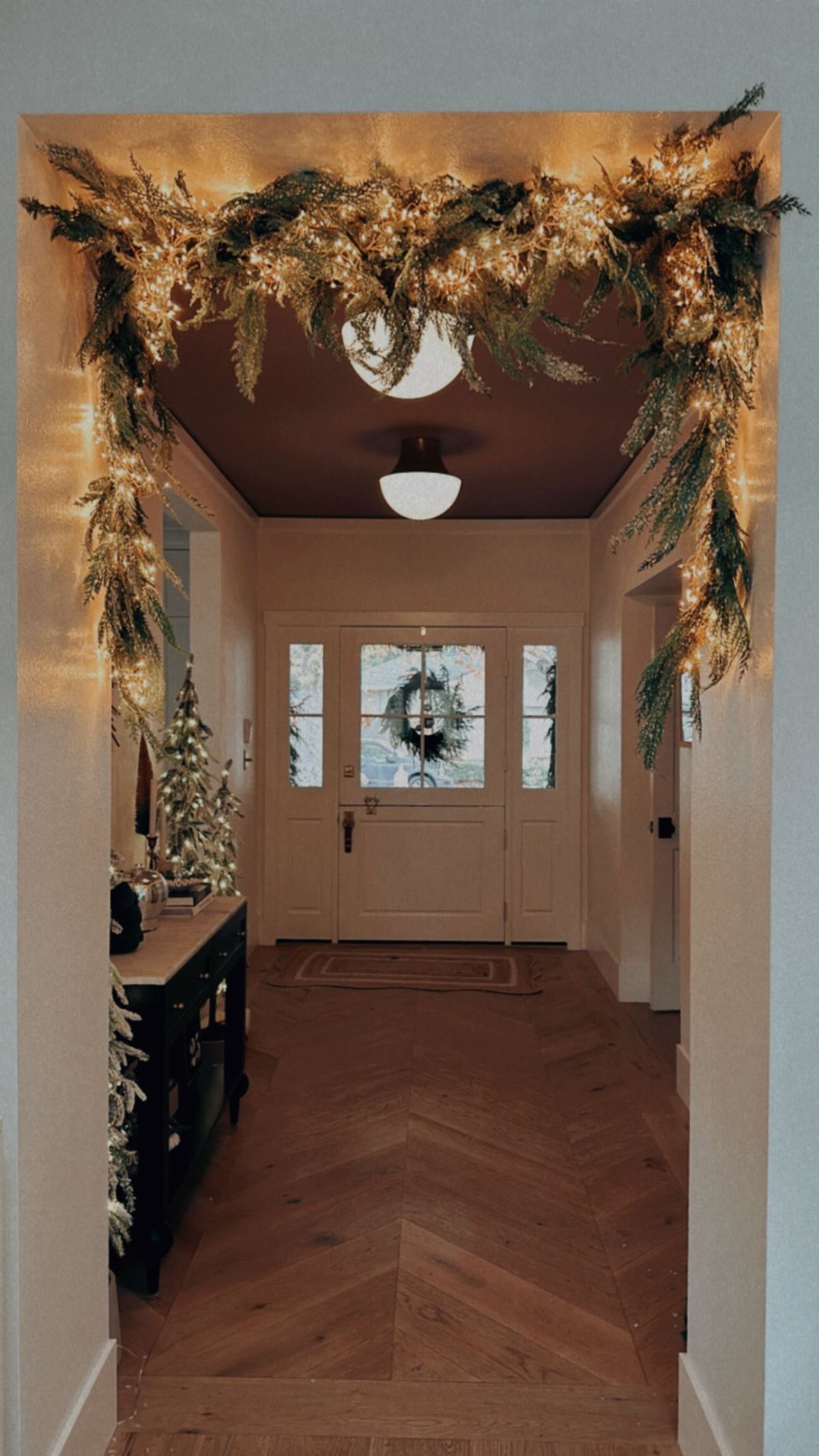 Lit evergreen garland draped over a doorway archway in a festive home entryway.