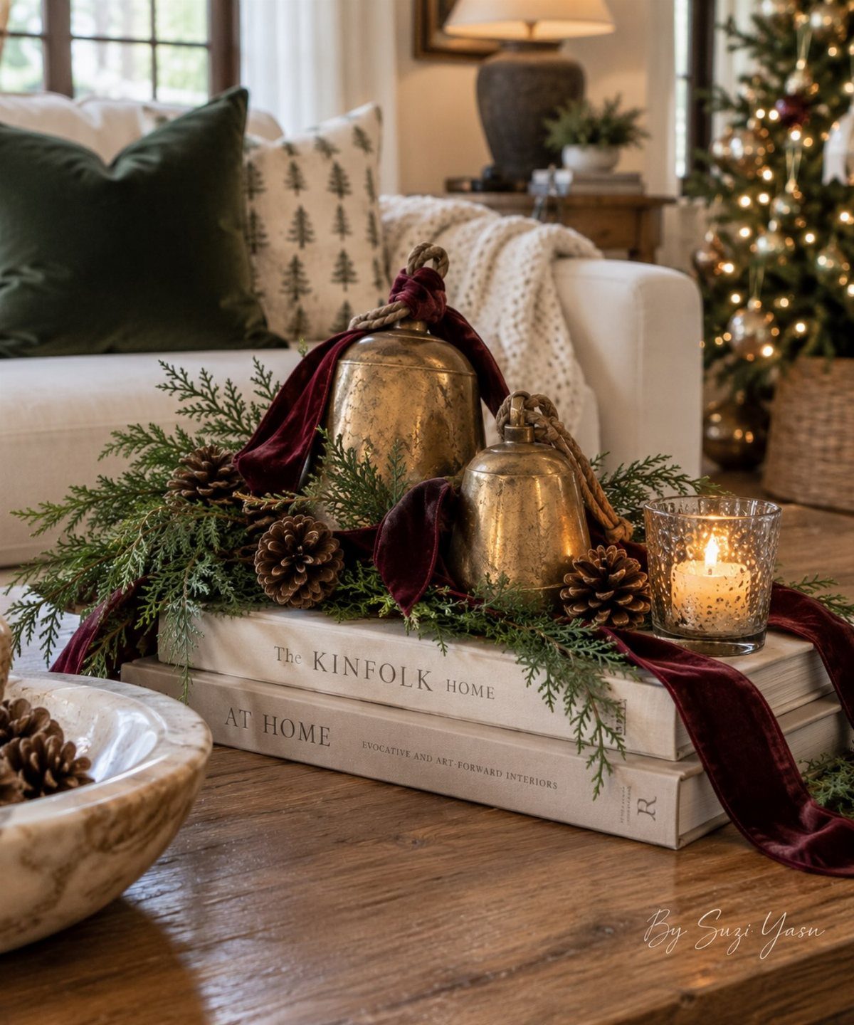 Brass bells, greenery, and a candle arranged on stacked books on a wooden table.