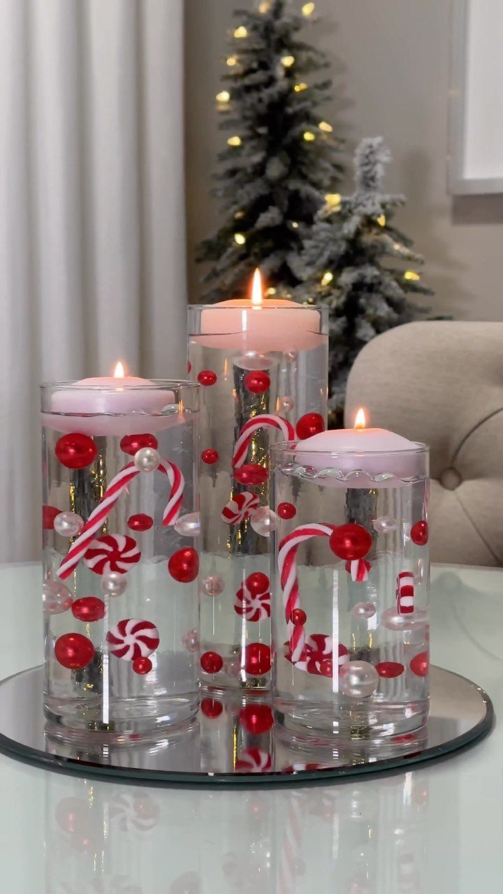Three lit pink floating candles in glass vases filled with candy canes and ornaments.
