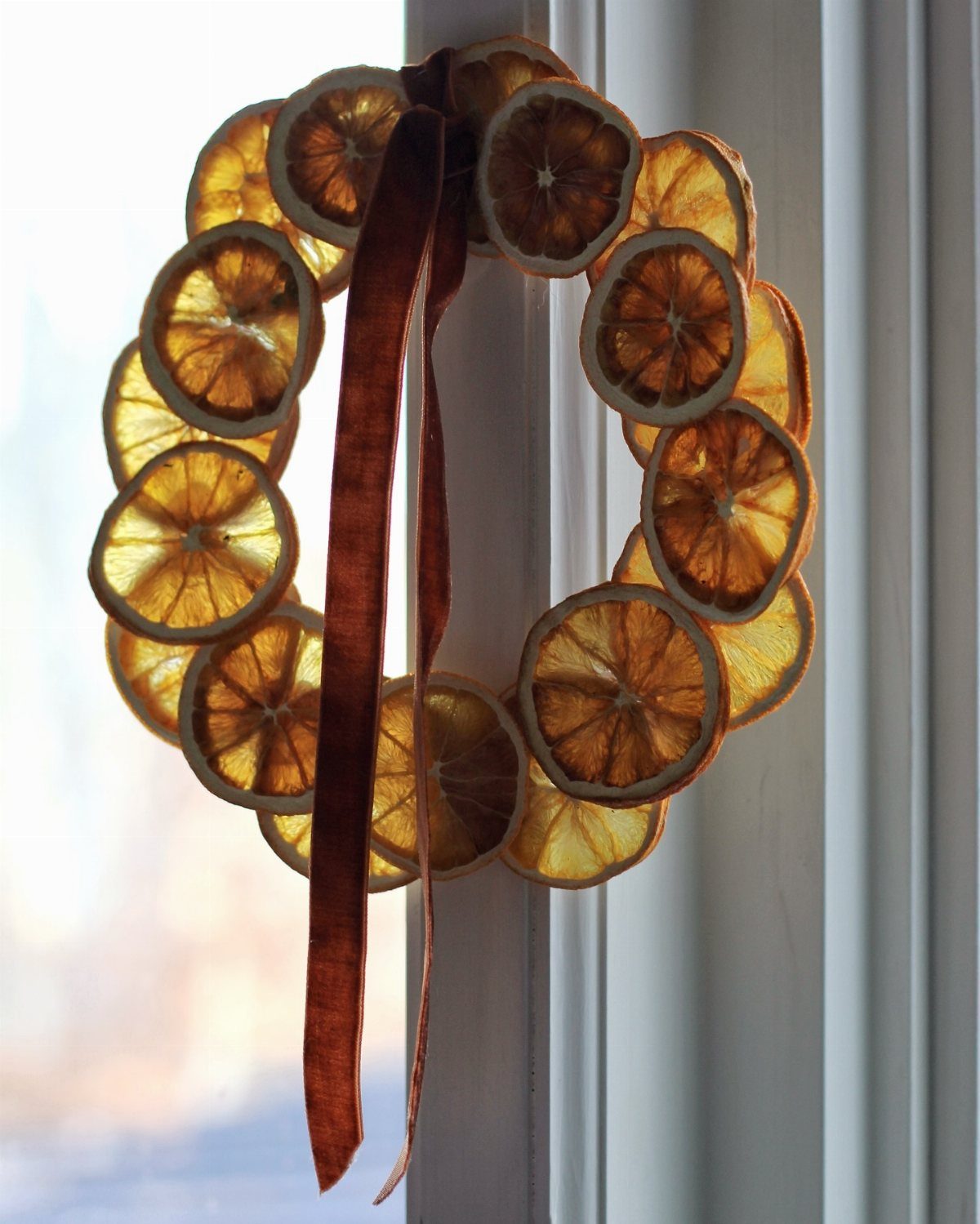 A wreath made of dried orange slices hanging on a white window frame with a velvet ribbon.